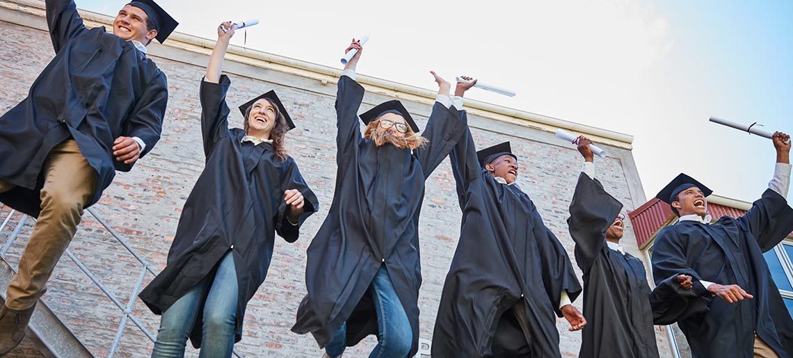 Low angle shot of a happy group of students jumping in celebration on graduation day.