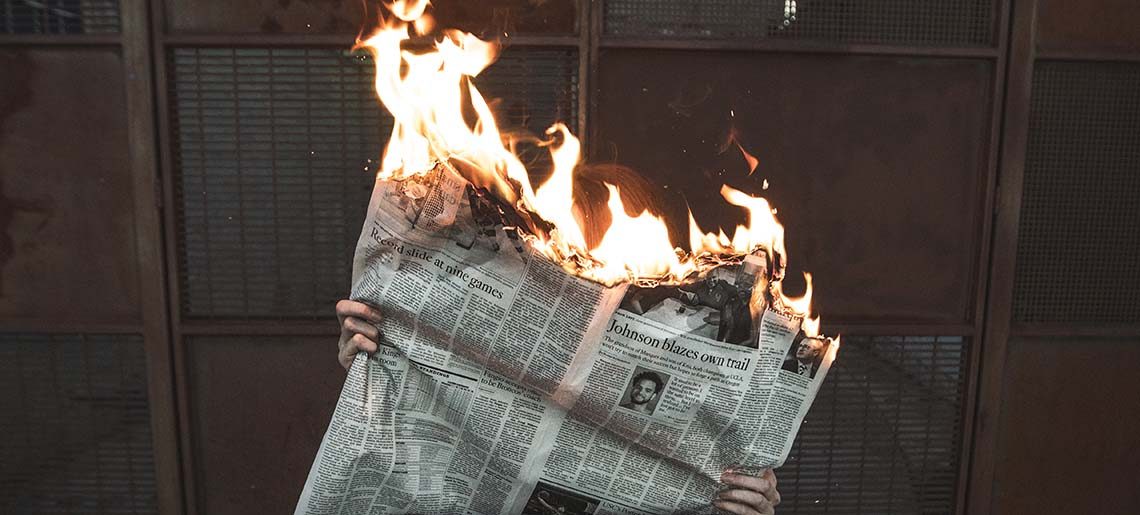 A vertical shot of a male sitting on a chair reading a burning newspaper 
Concept- Fake news